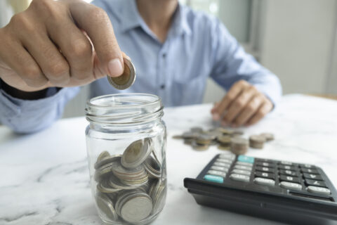 Businessman saving money concept. Hand holding coins putting in jug glass