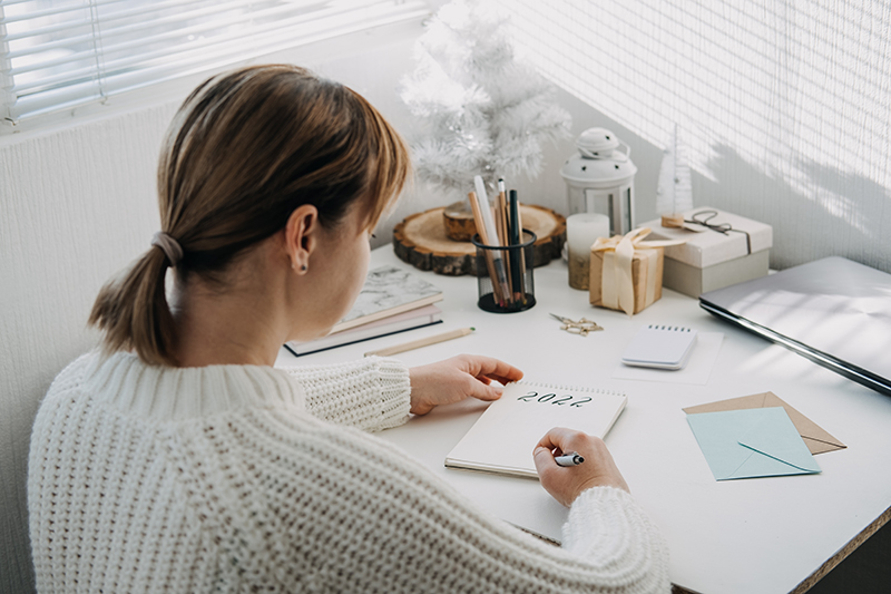 2022 goals, New year resolution. Woman in white sweater writing Text 2022 in open notepad on the table. Start new year, planning and setting goals for the next year